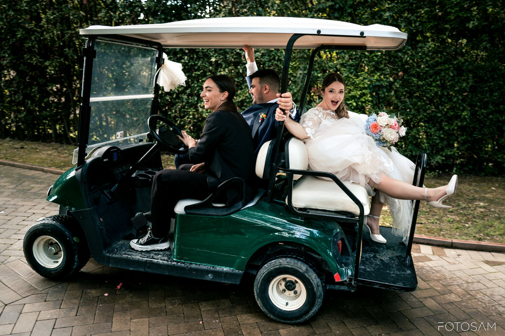 sposi sorridenti sul golf cart con bouquet durante le nozze a villa castellani