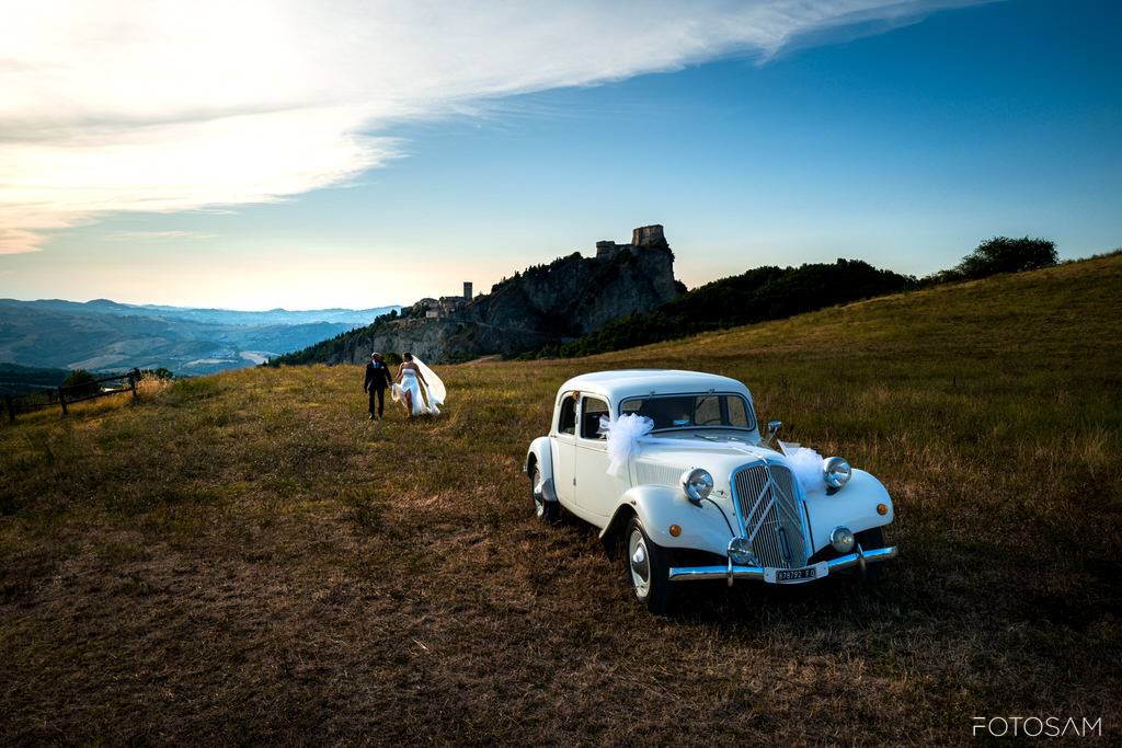 auto-depoca-bianca-nel-prato-con-la-rocca-di-san-leo-sullo-sfondo