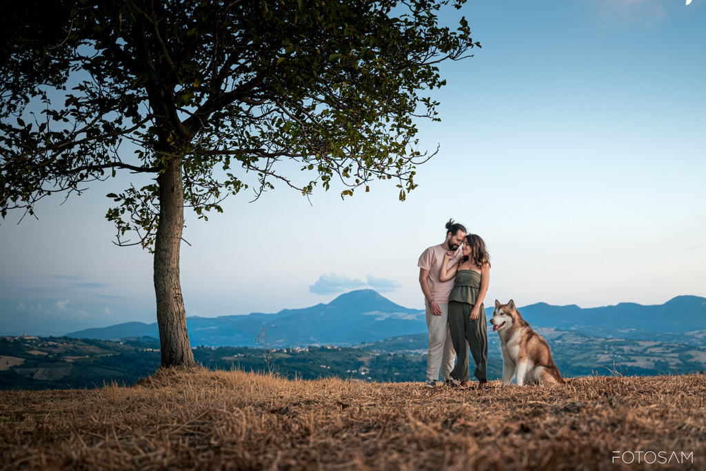coppia-in-piedi-con-il-cane-davanti-al-panorama-delle-colline-al-tramonto
