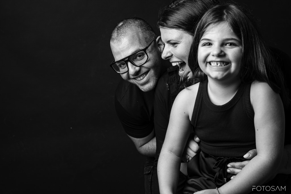 padre-madre-e-figlia-sorridenti-in-studio-su-sfondo-scuro-in-una-scena-intima-e-naturale