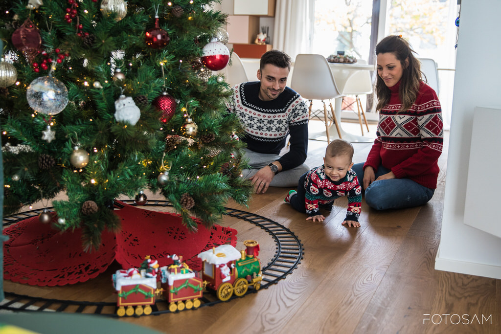 famiglia-seduta-vicino-albero-decorato-bambino-gioca-con-genitori-trenino-palline