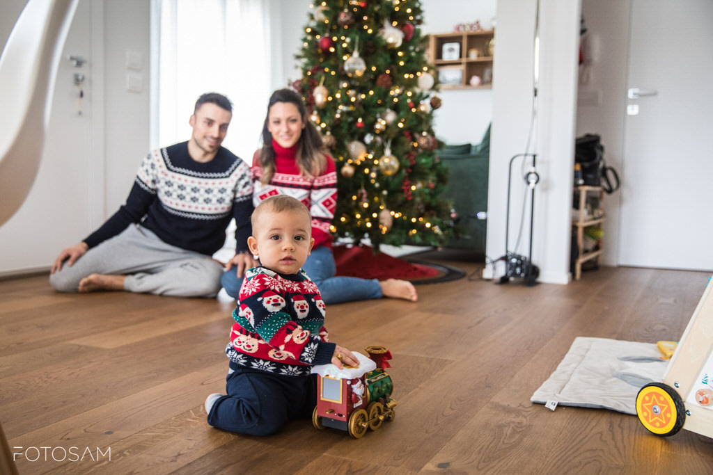 genitori-sorridenti-guardano-il-bambino-giocare-sotto-albero-addobbato