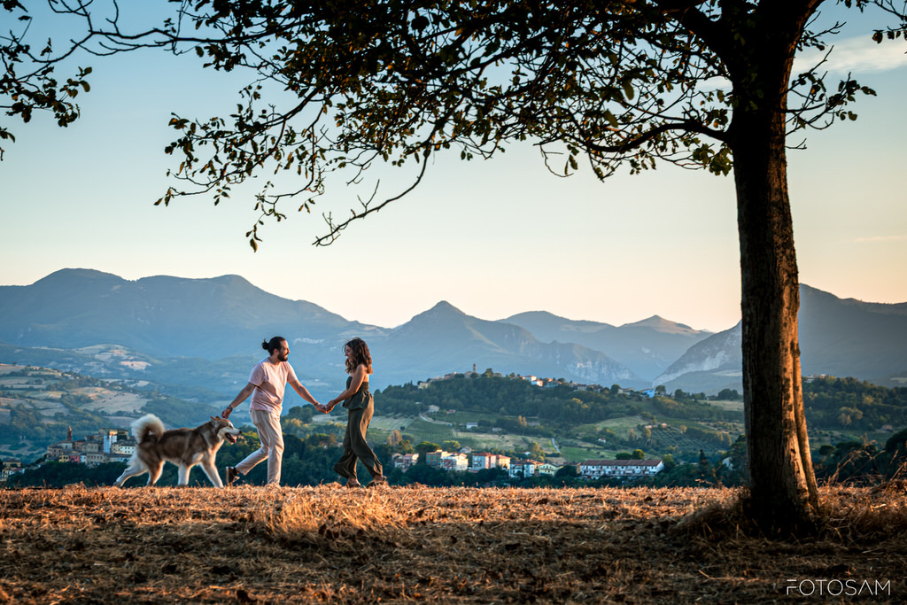 coppia-che-cammina-con-il-cane-in-un-campo-con-le-montagne-sullo-sfondo