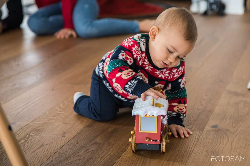 bambino-con-maglione-natalizio-che-gioca-con-il-trenino-rosso-davanti-ai-genitori