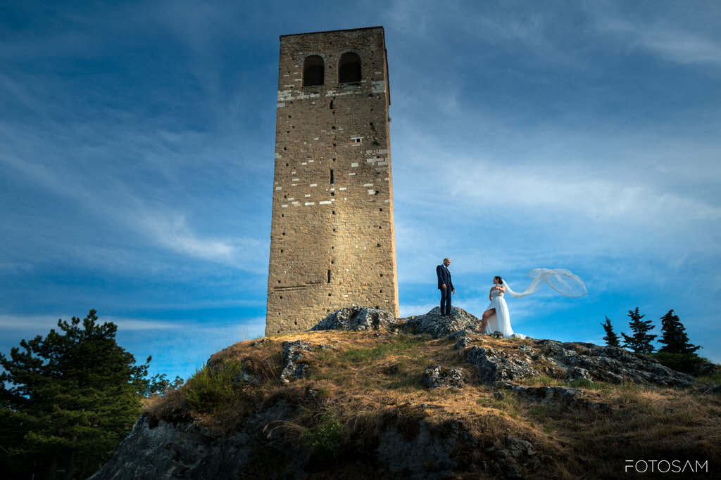 sposi-in-piedi-sulla-collina-con-la-rocca-di-san-leo-sullo-sfondo