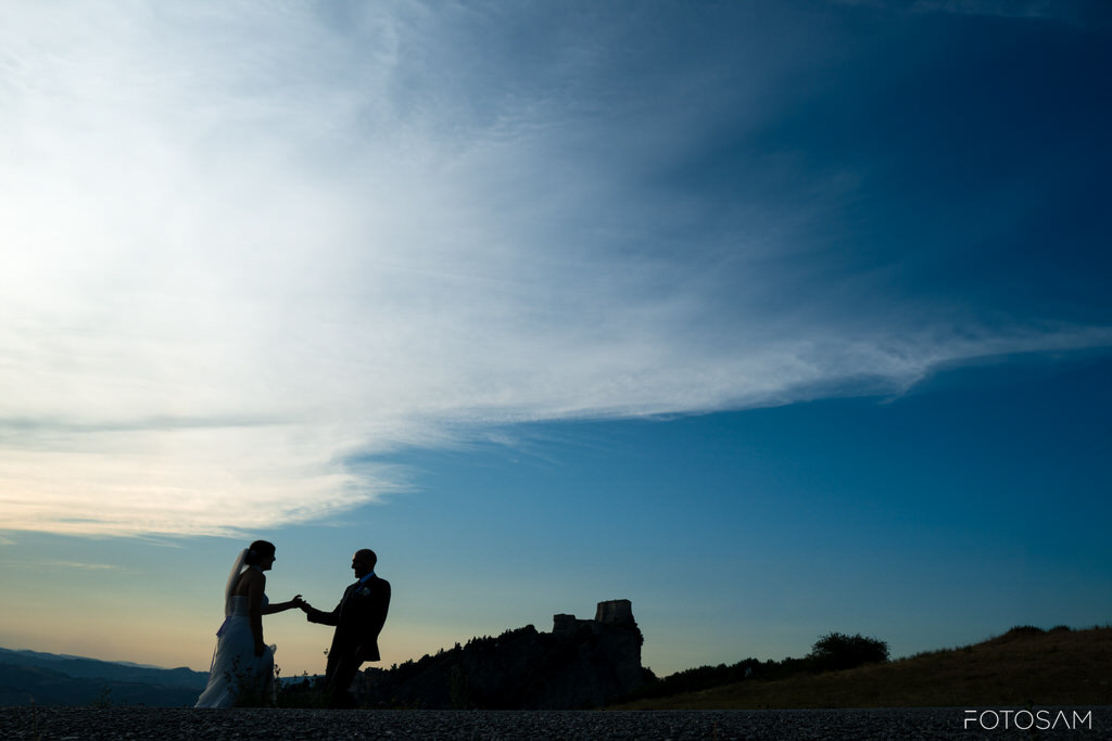 sposi-che-si-tengono-per-mano-al-tramonto-davanti-alla-rocca-di-san-leo