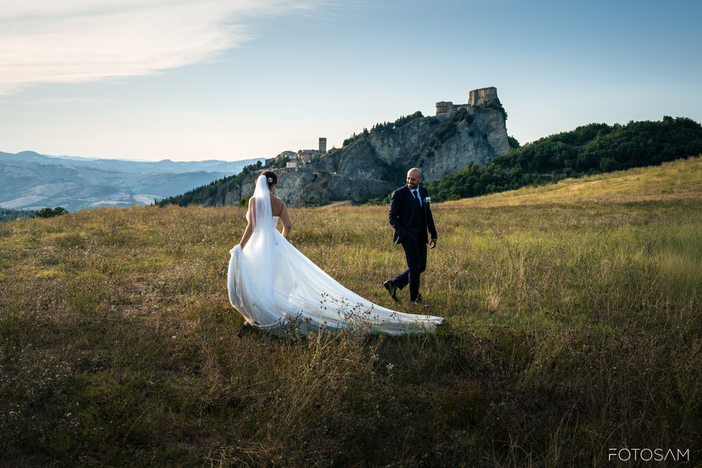 sposa-con-velo-lungo-nel-prato-con-la-rocca-di-san-leo-sullo-sfondo