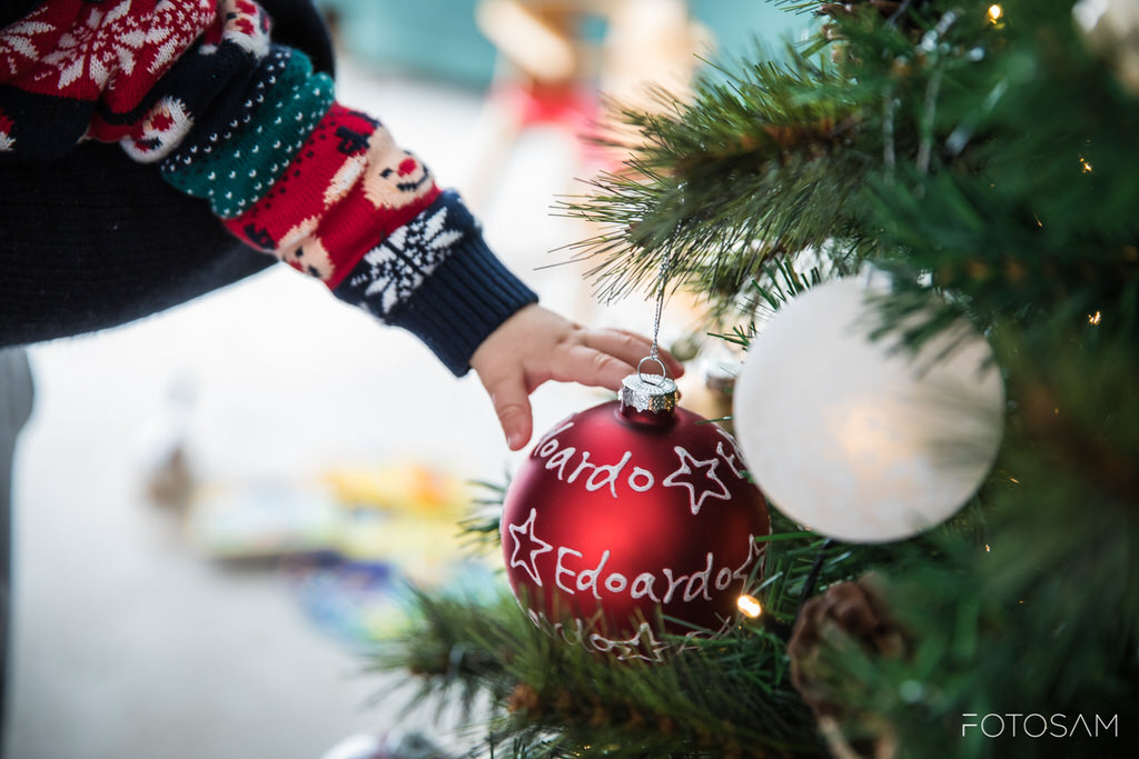 mano-bambino-appende-pallina-decorata-con-nome-nell-albero-acceso